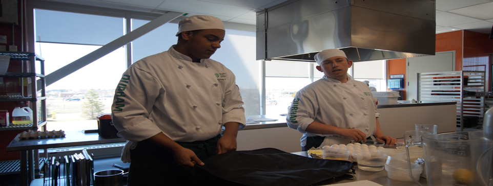 Two male students in chef outfits in a kitchen