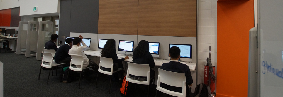 Students sitting by a wall of Mac computers